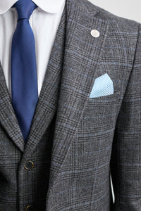 Terno xadrez cinza com gravata azul e lenço de bolso sobre fundo cinza claro.