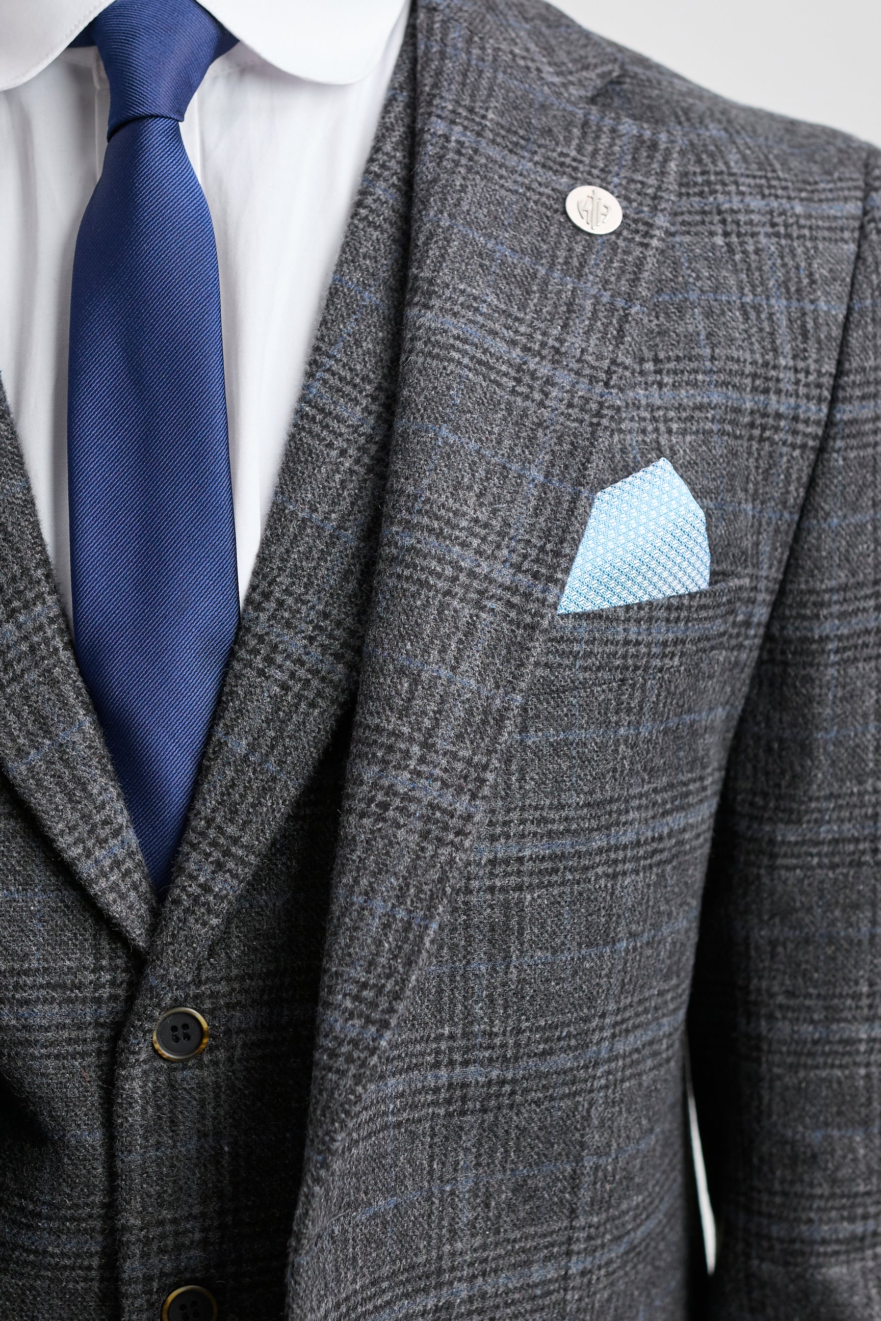 Terno xadrez cinza com gravata azul e lenço de bolso sobre fundo cinza claro.