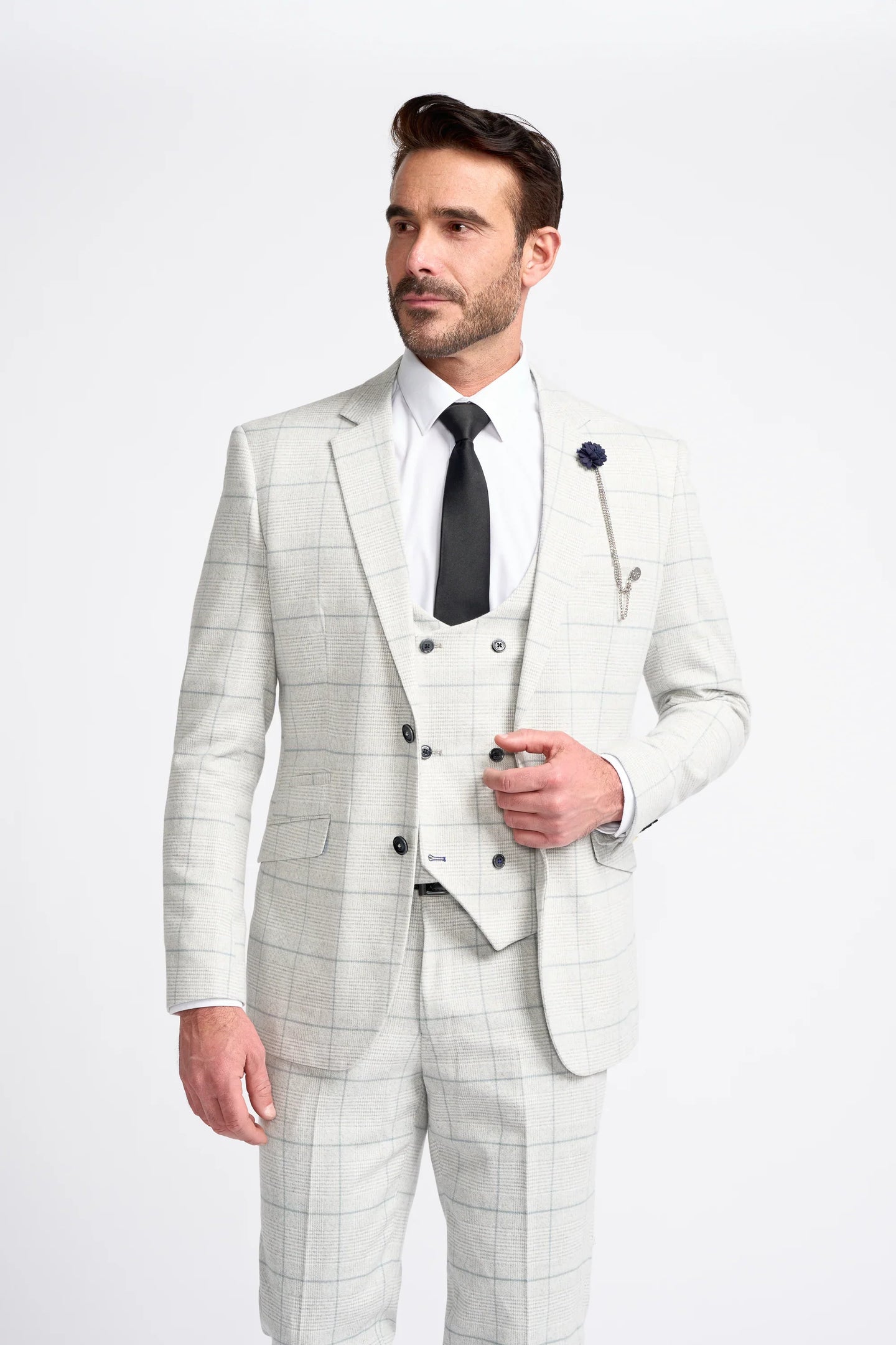 Homem vestindo um terno xadrez cinza claro com camisa branca e gravata preta sobre um fundo branco.