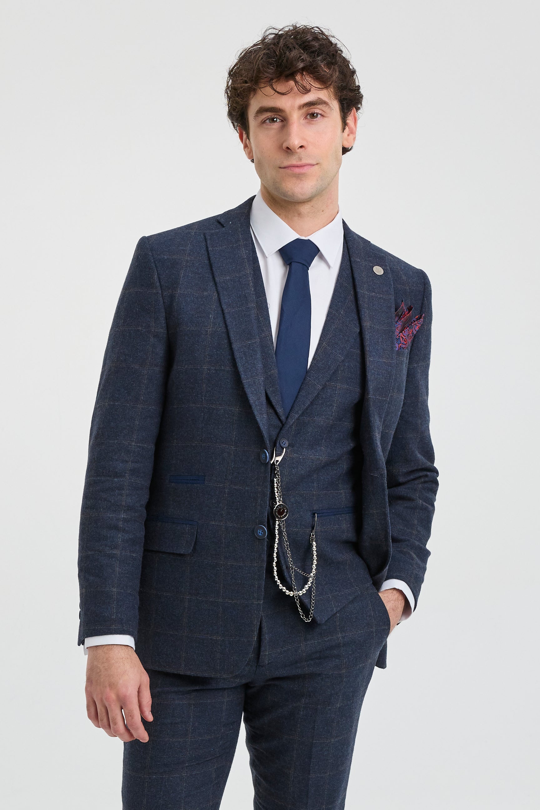 Homem vestindo um terno xadrez azul com camisa branca e gravata azul sobre um fundo cinza claro.