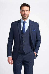 Homem vestindo terno azul-marinho com camisa branca e gravata azul sobre um fundo cinza claro.