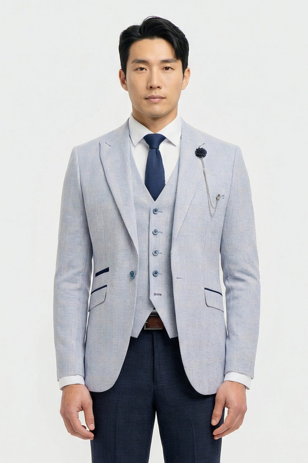 Homem vestindo blazer cinza claro, colete azul-marinho e gravata azul-escura sobre um fundo branco.