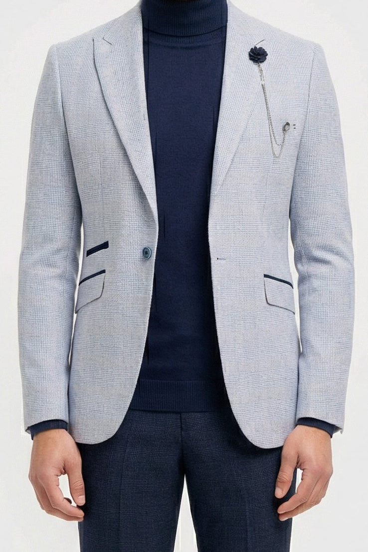 Homem vestindo blazer cinza claro, gola alta azul-marinho e calça escura sobre um fundo branco.