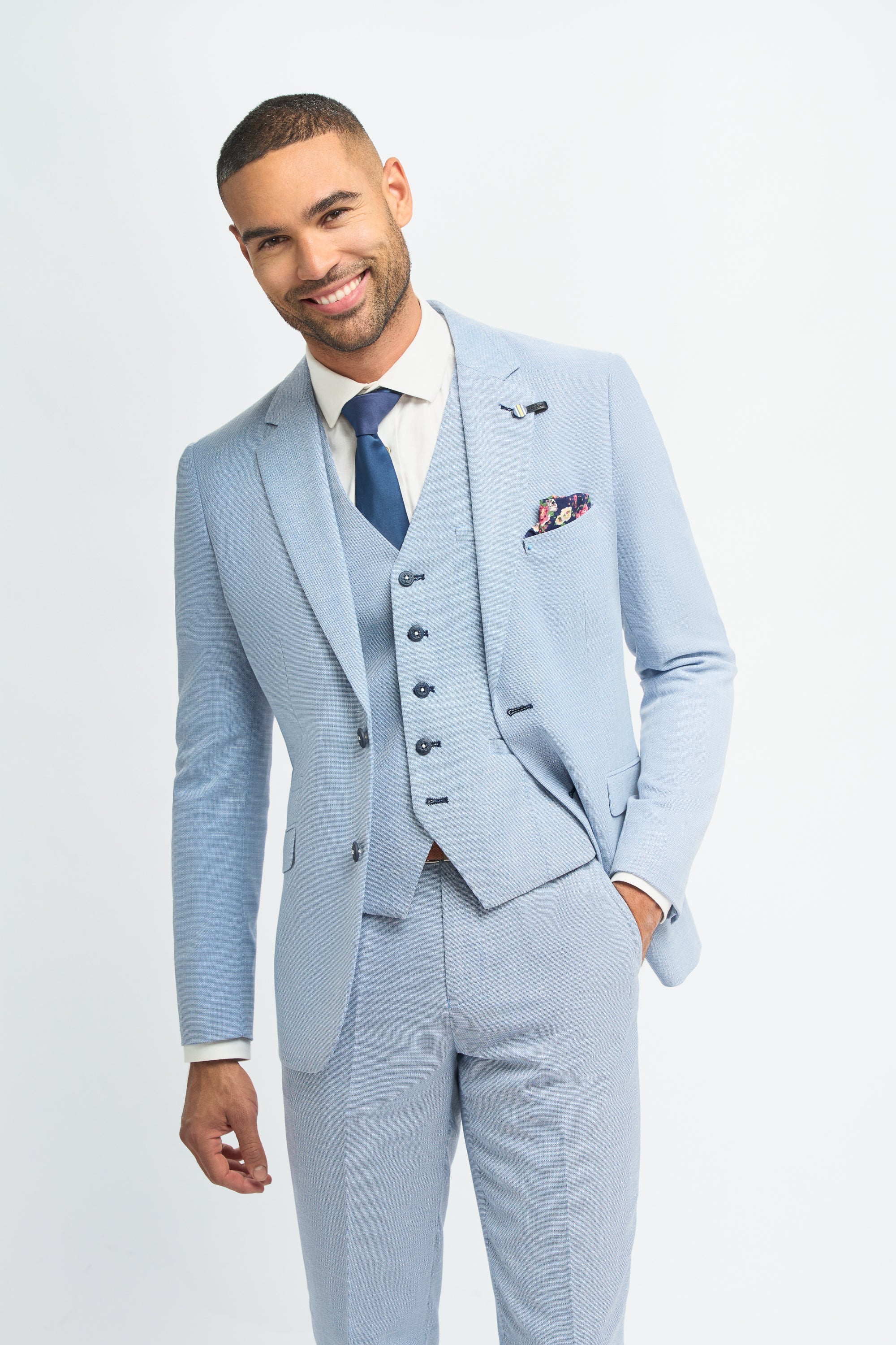 Homem vestindo terno azul claro com camisa branca e gravata azul sobre um fundo liso.